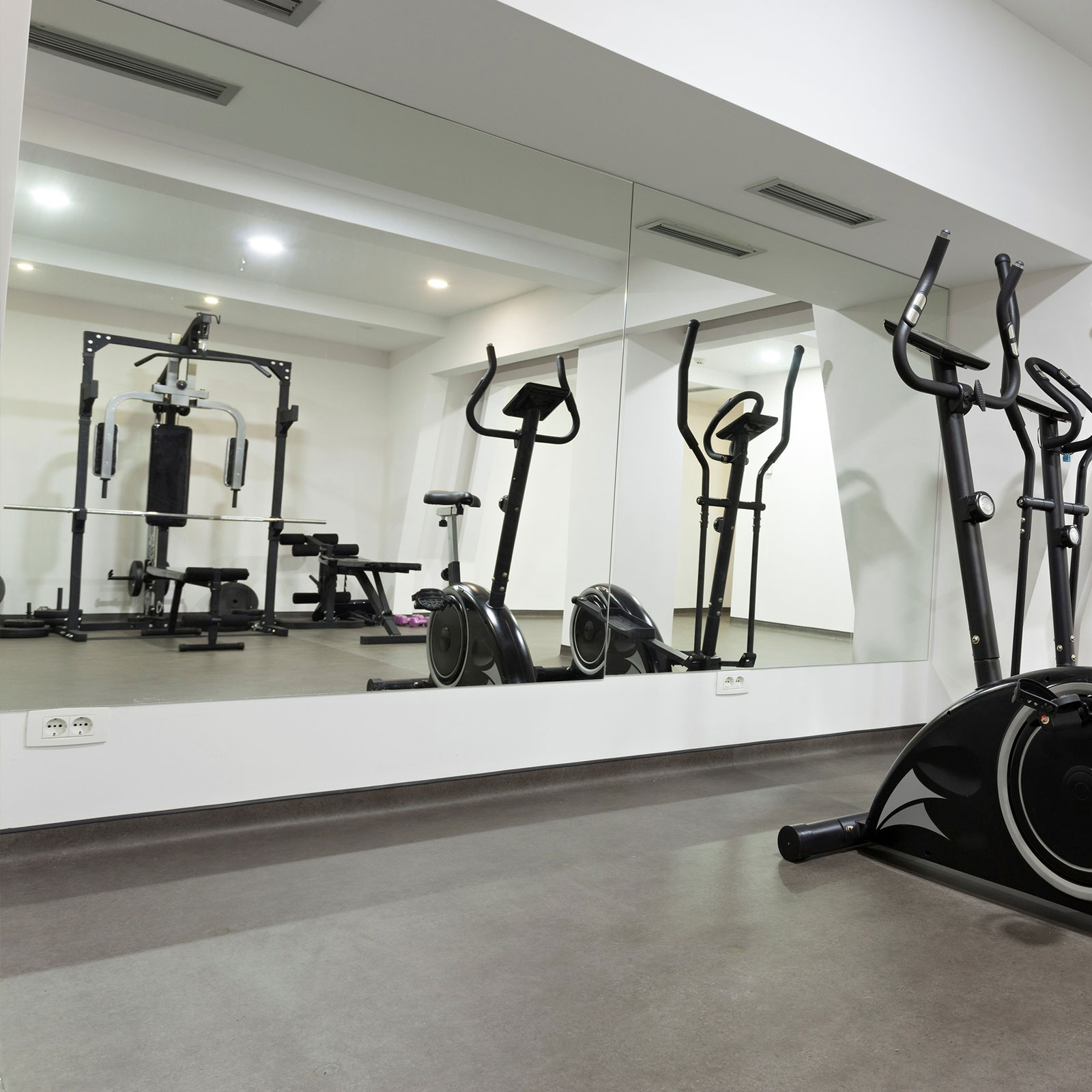 Der Raum eines Fitnessstudios, mit großem Spiegel, in dem sich die Trainingsgeräte spiegeln.